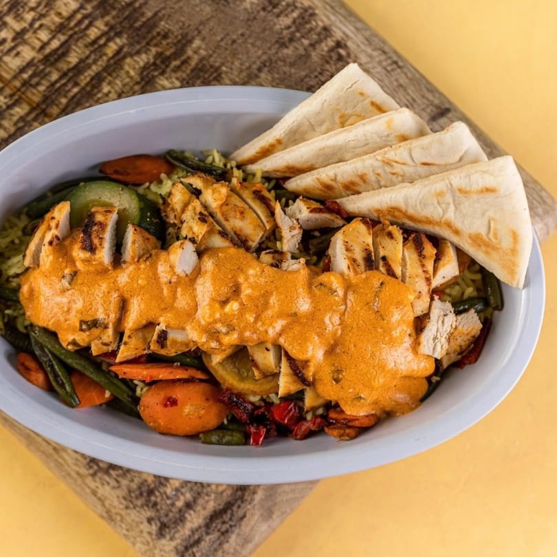 Daphne's Greek Cafe's grilled chicken with orange sauce, vegetables, and pita bread in a bowl.