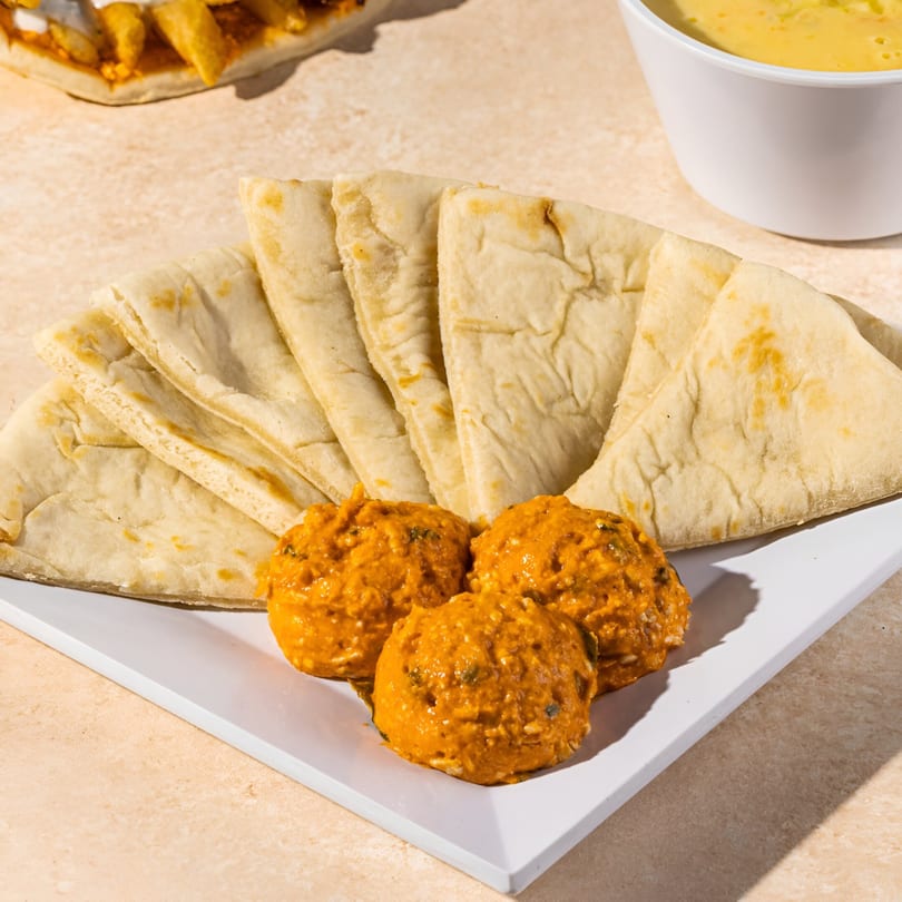Pita bread triangles and three scoops of orange dip on a white plate, with a yellow dip in a bowl.